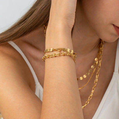 Bracelet en acier inoxydable doré avec chaînes multiples et disques ronds brillants, porté au poignet féminin.
