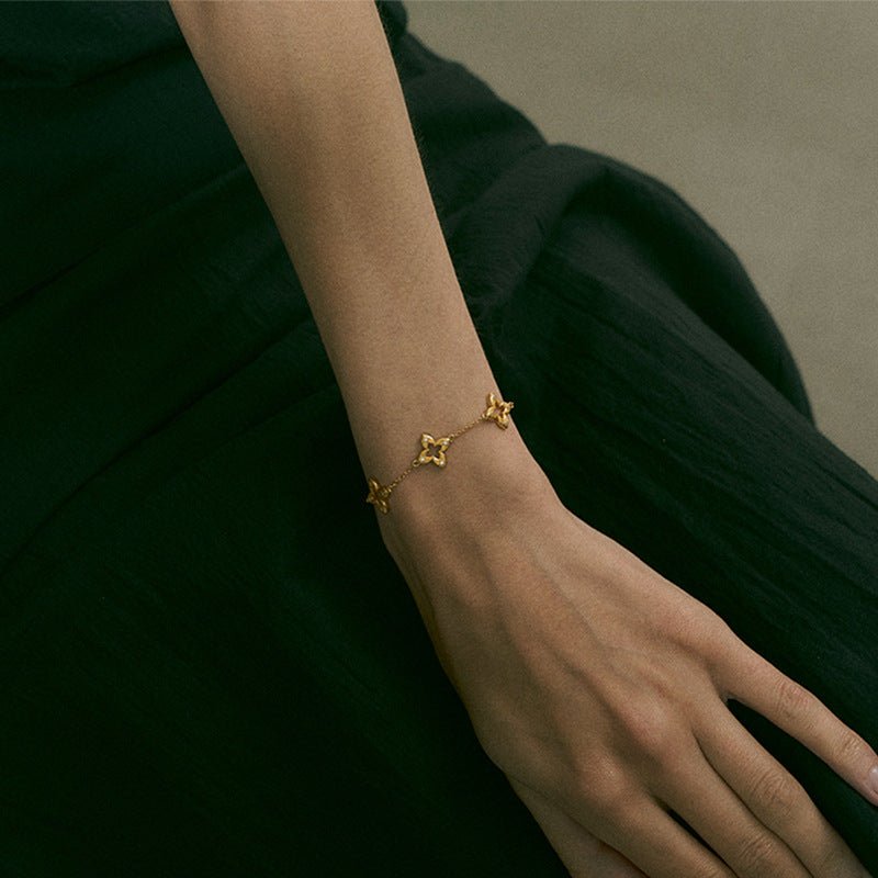 Bracelet fin doré en titane avec trois trèfles ajourés et petits éclats de zircon sur chaîne délicate.