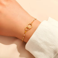 Bracelet fin en or avec deux anneaux entrelacés et chaîne délicate sur poignet féminin.
