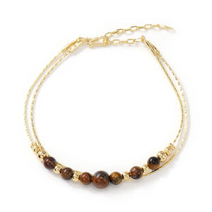 Bracelet double chaîne fine dorée avec perles rondes en œil de tigre brun, style minimaliste élégant.