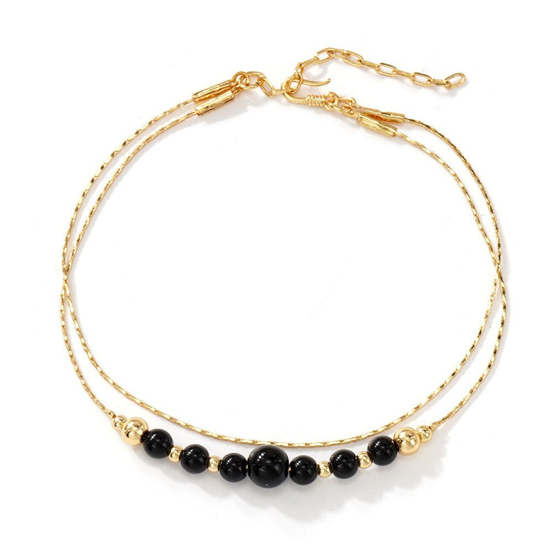 Bracelet double chaîne dorée avec perles noires en onyx, design minimaliste élégant.
