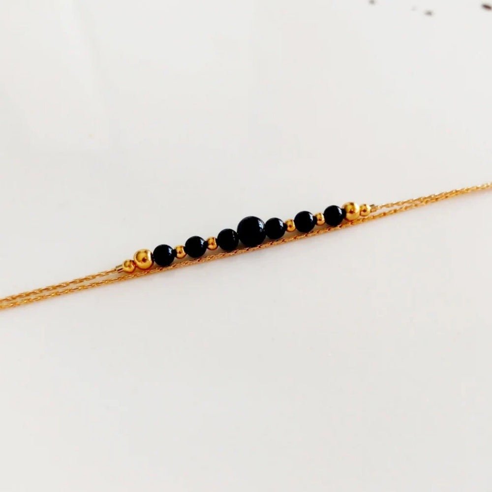 Bracelet double chaîne fine dorée avec perles noires en onyx, style minimaliste élégant.
