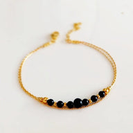 Bracelet double chaîne dorée avec perles noires en onyx lisse et élégantes petites boules dorées.