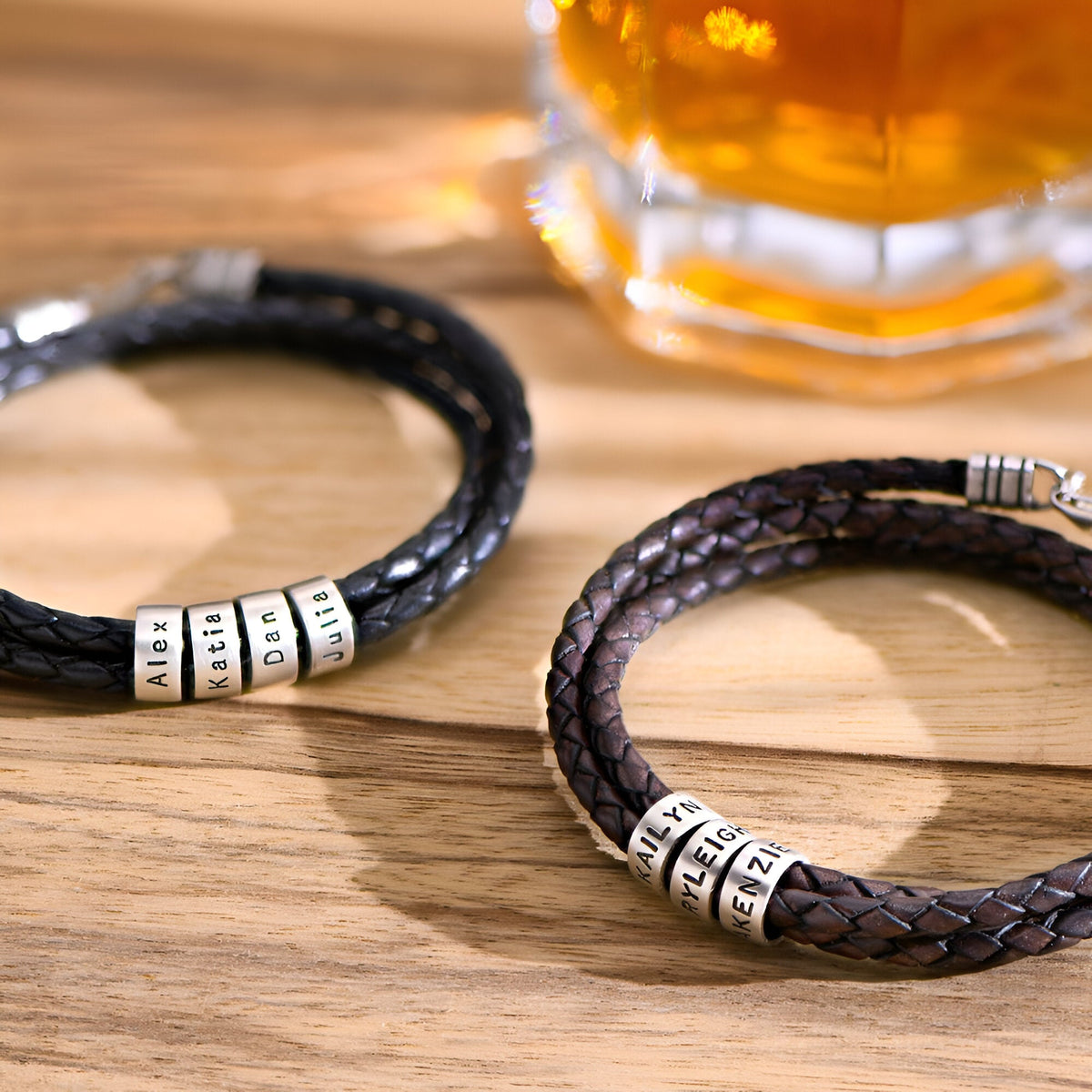 Bracelet double cordon en cuir noir tressé avec deux plaques métalliques arrondies gravées.
