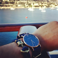 Bracelet double cordon bleu et blanc avec motif ancre antique en métal doré porté au poignet.