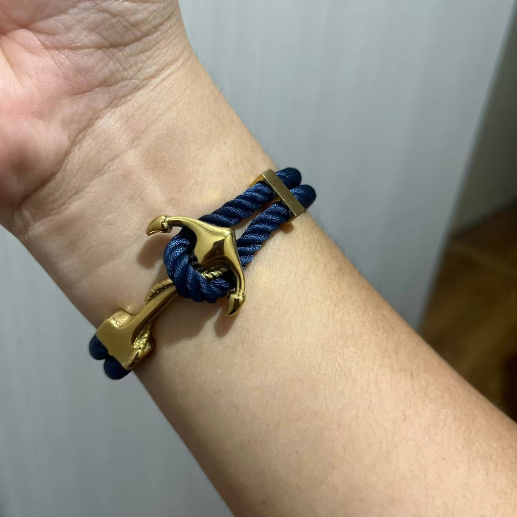 Bracelet double cordon bleu marine avec motif ancre dorée en métal brillant.
