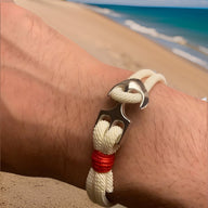Bracelet double cordon blanc avec motif ancre large en métal argenté et détail rouge au bord.