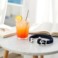 Bracelet double cordon bleu marine avec motif ancre argentée posé sur table en marbre blanc.