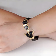 Bracelet homme double cordon cuir noir avec ancre dorée et boussole centrale sur fond noir.