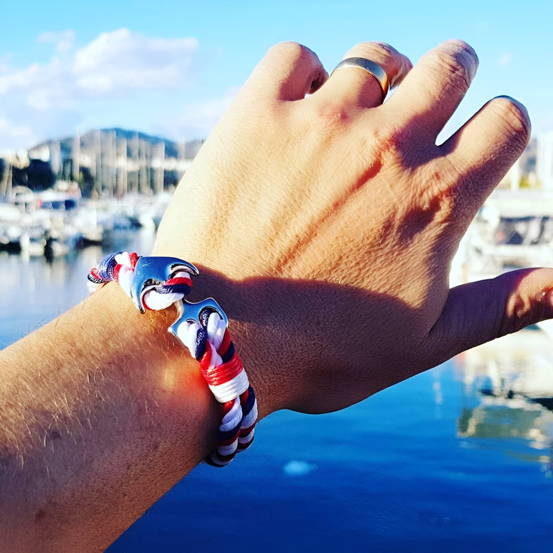 Bracelet double cordons bleu blanc rouge avec ancre marine argentée sur poignet masculin.