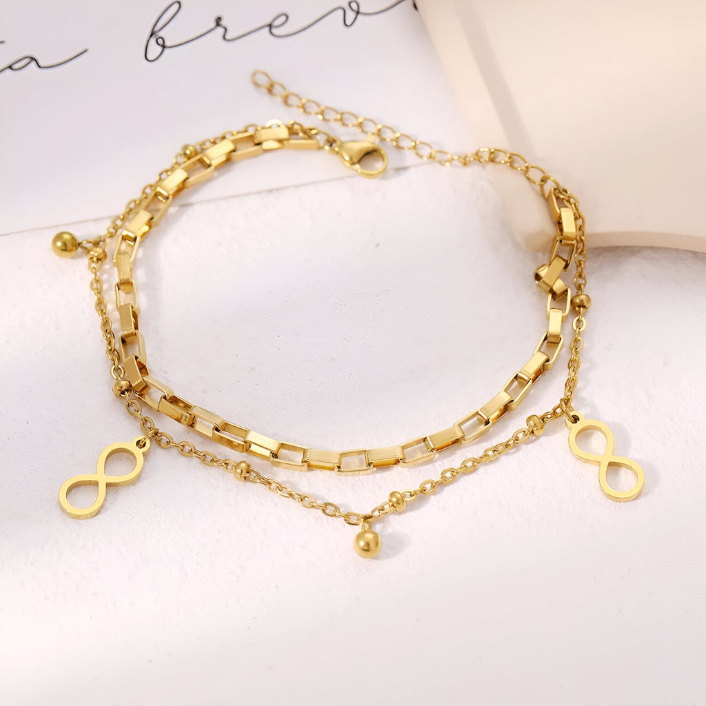 Bracelet double chaîne en acier inoxydable doré avec charms infini et pendentif boule délicat.