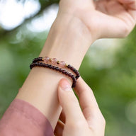 Bracelet double en perles de grenat rouge et quartz rose porté au poignet féminin, fond flou végétal.
