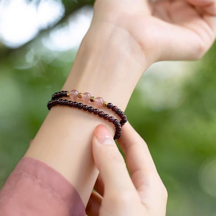 Bracelet double en perles de grenat rouge et quartz rose porté au poignet féminin, fond flou végétal.