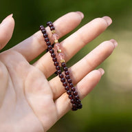 Bracelet double en perles de grenat rouge et quartz rose avec petites boules dorées, porté sur main féminine.