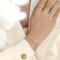 Bracelet double rang en titane plaqué or, finition lisse et chaîne fine élégante, porté au poignet féminin.