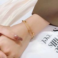 Bracelet double en titane plaqué or à motif petits cubes porté au poignet féminin, design minimaliste et élégant.