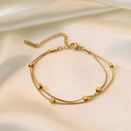 Bracelet double en titane plaqué or avec petits cubes géométriques sur fil fin et chaîne réglable.