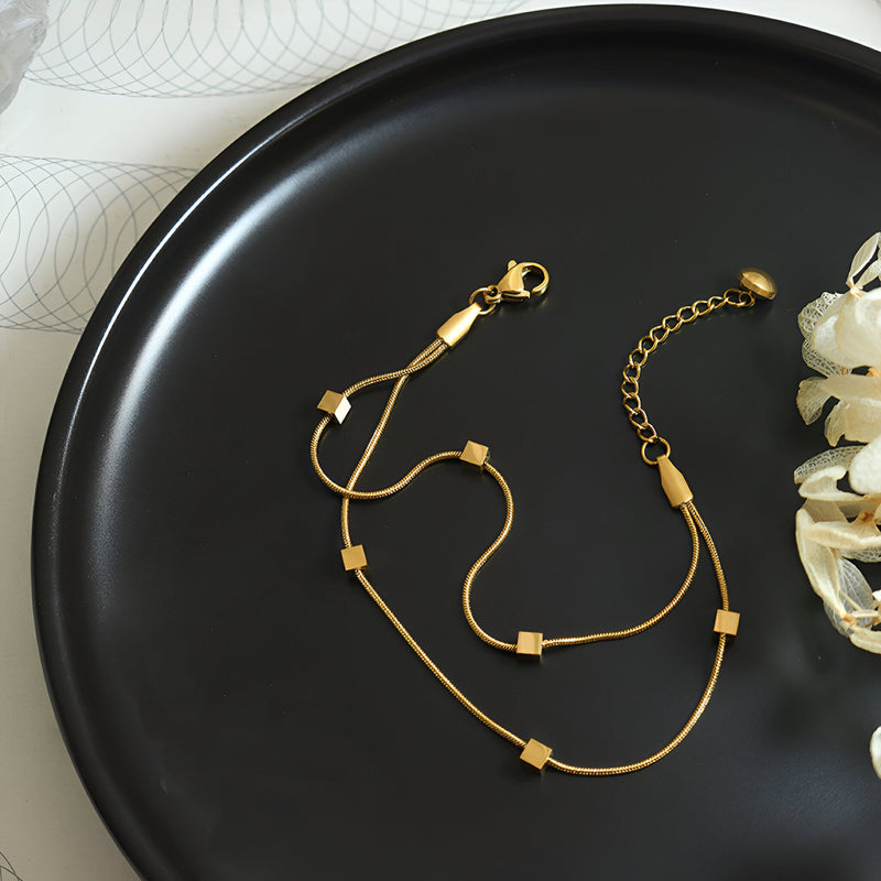 Bracelet double en titane plaqué or avec motif petits cubes et fermoir mousqueton sur plaque noire.