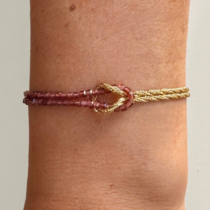 Bracelet double rang perles rouges et corde dorée torsadée avec fermoir mousqueton et nœud lumineux.