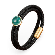 Bracelet double-rangs en cuir tressé noir avec pierre verte scintillante et fermoir doré mat.
