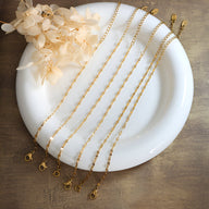 Ensemble de bracelets fins en titane plaqué or, chaînes délicates avec fermoirs mousqueton sur assiette blanche.