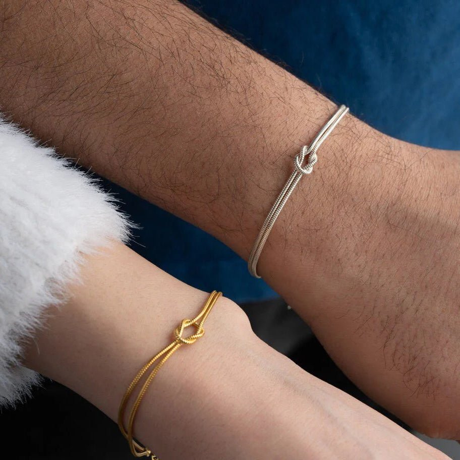 Bracelet en acier inoxydable argenté à nœud central fin sur poignet masculin et bracelet doré fin avec nœud central sur.