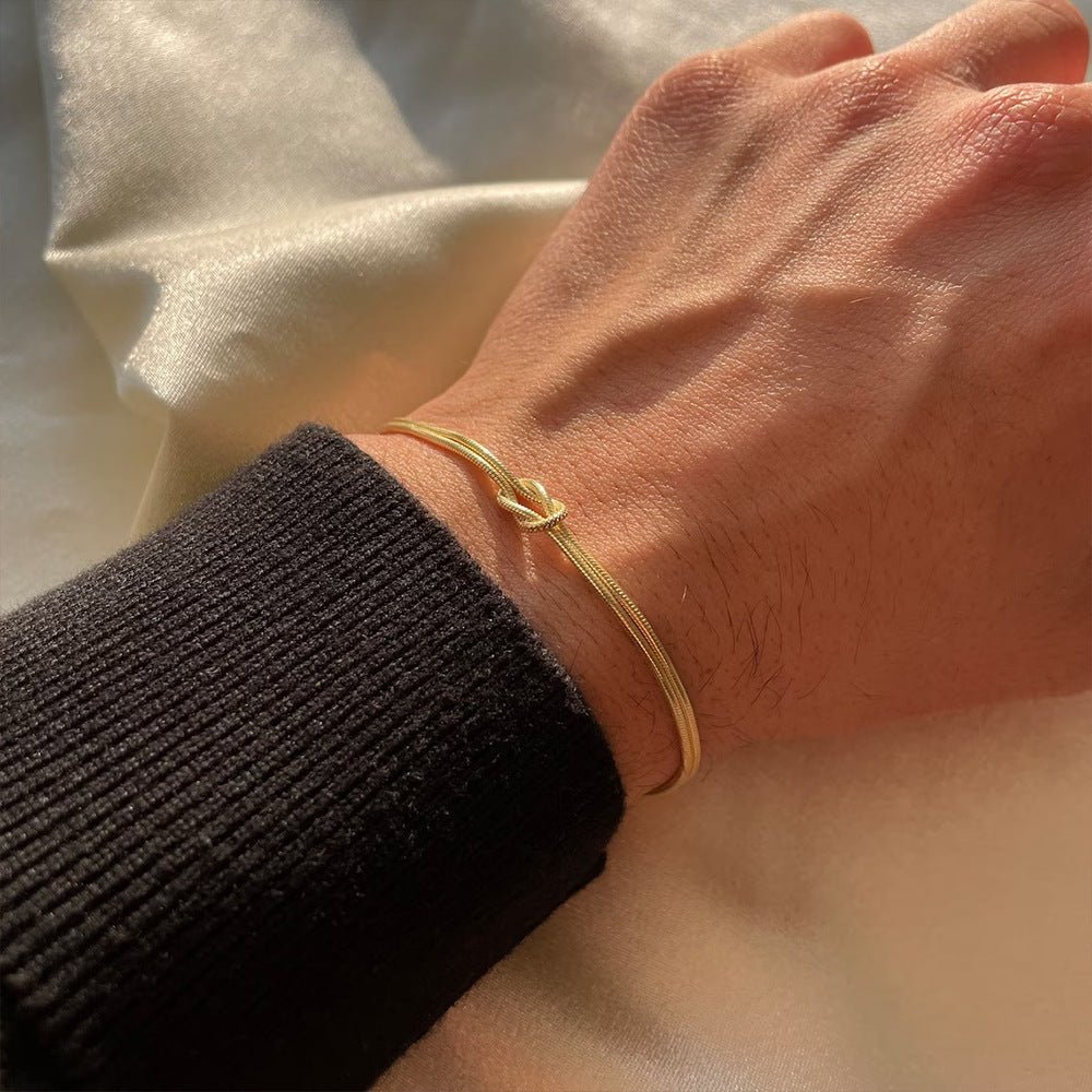 Bracelet fin en acier inoxydable doré avec nœud central minimaliste, style élégant et moderne.