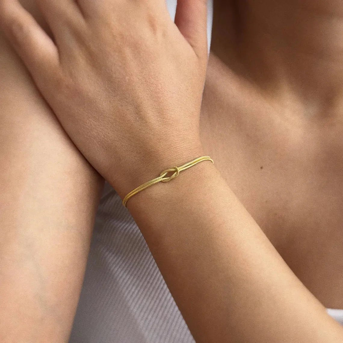 Bracelet fin en acier inoxydable doré avec nœud central minimaliste, style délicat et élégant pour femme.