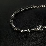 Bracelet homme en acier inoxydable et hématites noires avec charm ancre argenté sur fond noir.