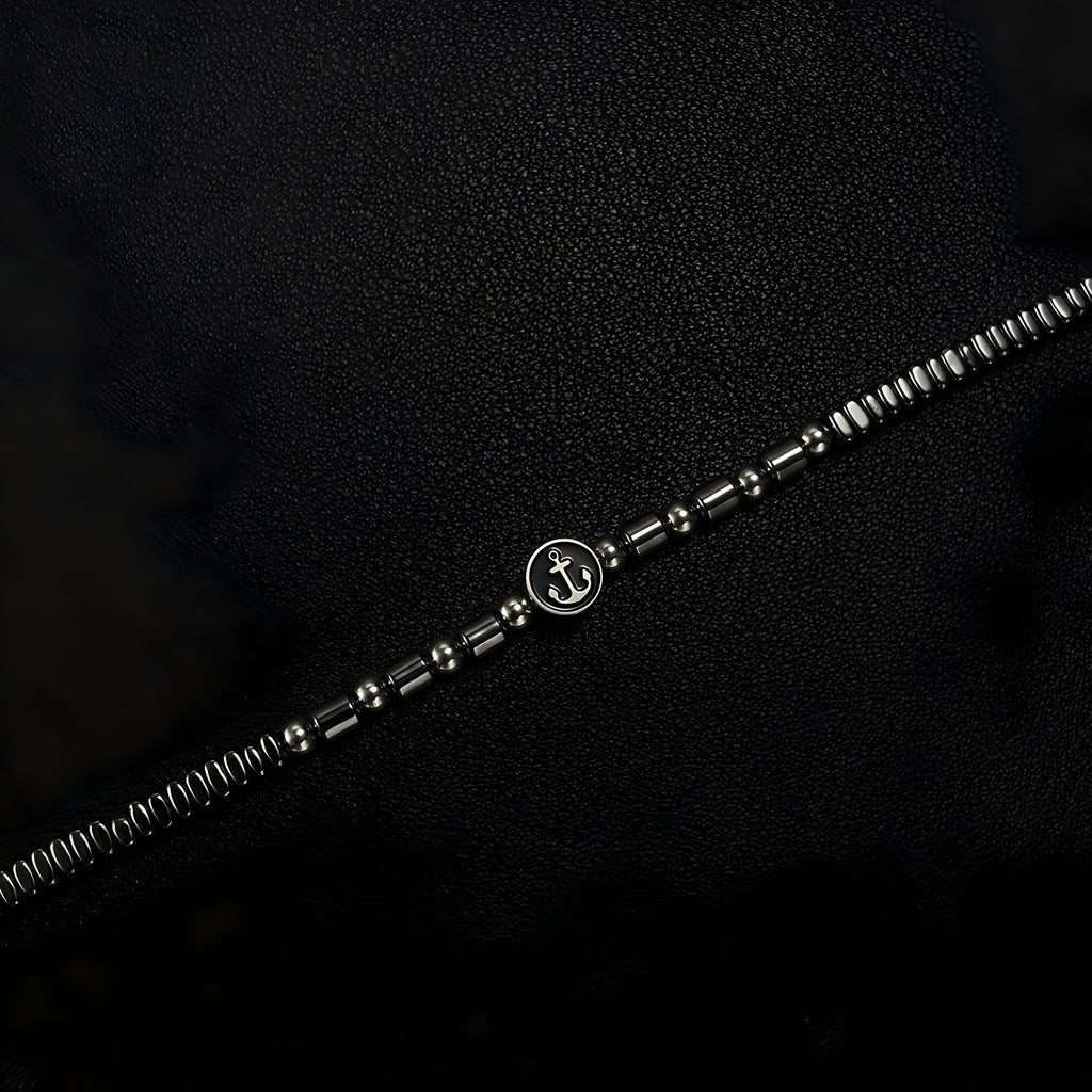 Bracelet homme en acier inoxydable argenté avec perles hématites noires et charm ancre au centre.