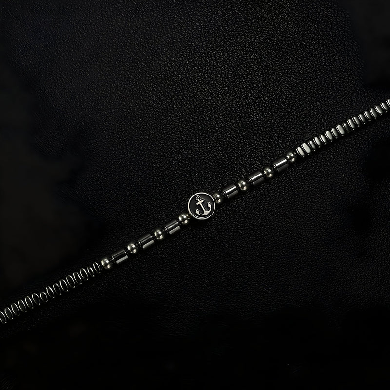 Bracelet homme en acier inoxydable argenté avec perles hématites noires et charm ancre au centre.