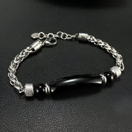 Bracelet homme en acier inoxydable argenté avec pierre d'œil de tigre noire allongée et détails texturés.