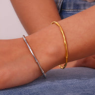 Bracelet fin en acier inoxydable plaqué or 18 carats style bambou porté au poignet femme, aussi en argent visible.