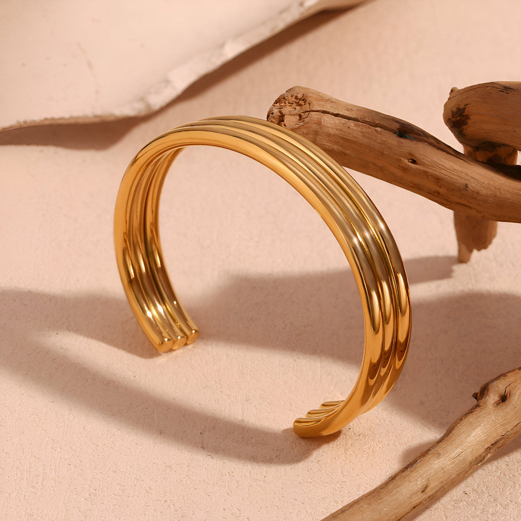 Bracelet jonc ouvert en acier inoxydable plaqué or 18 carats avec trois anneaux lisses entrelacés.