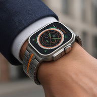 Bracelet en acier inoxydable gris avec bande orange pour Apple Watch, ajustable, style robuste et moderne.