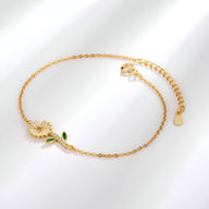 Bracelet fin en or avec charm marguerite détaillé et petites feuilles vertes en émail.