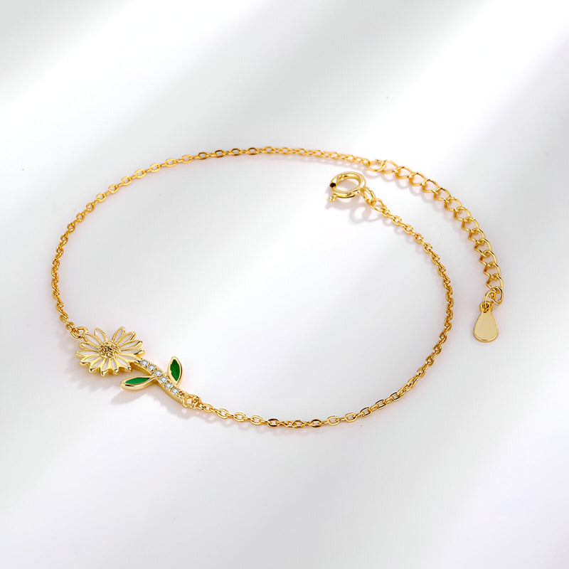 Bracelet fin en or avec charm marguerite détaillé et petites feuilles vertes en émail.