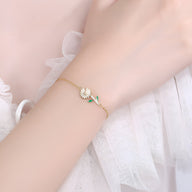 Bracelet fin en or avec charm marguerite émaillée blanche et tige verte délicate.