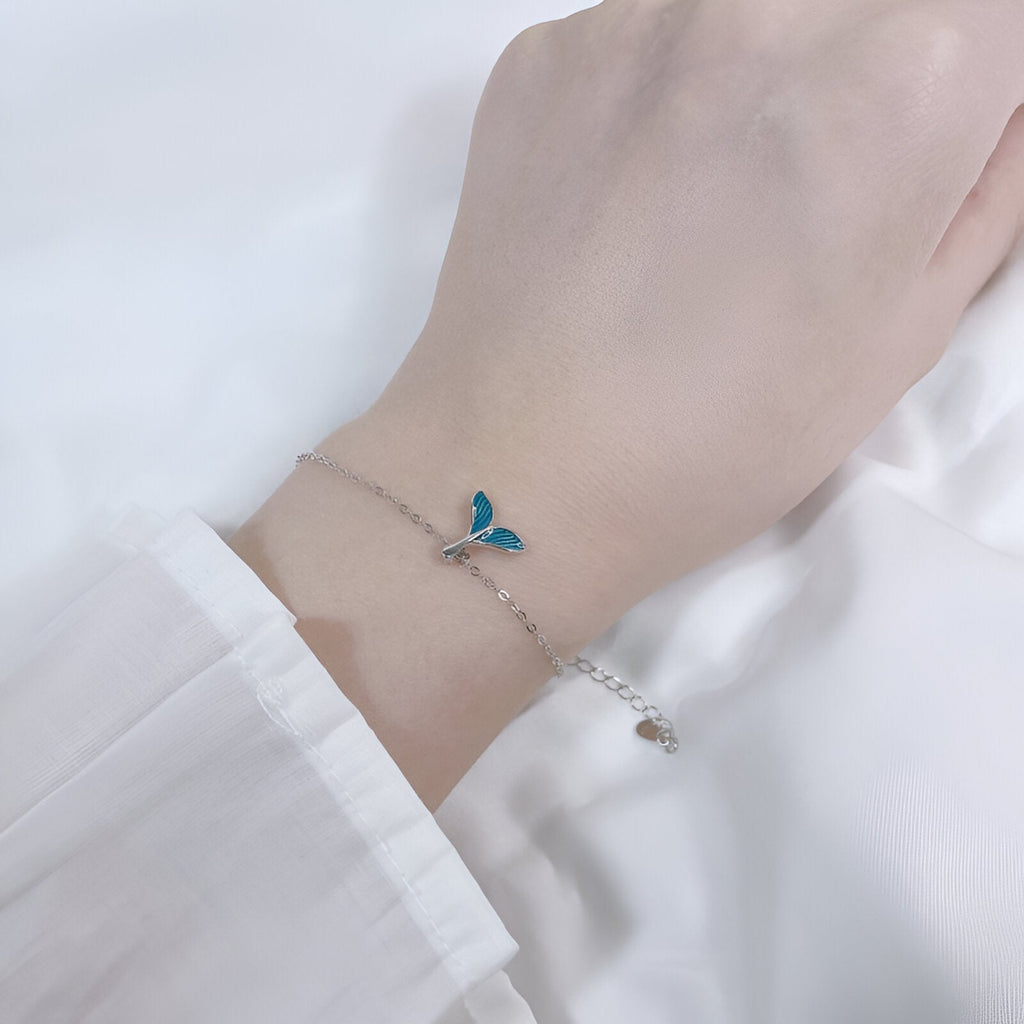 Bracelet en argent avec charm queue de baleine bleu sur poignet féminin, style délicat et minimaliste.
