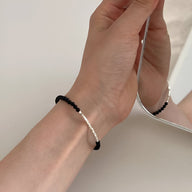 Bracelet fin en argent sterling avec perles d'onyx noir sur poignet féminin face à un miroir.