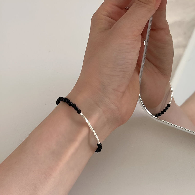 Bracelet fin en argent sterling avec perles d'onyx noir sur poignet féminin face à un miroir.