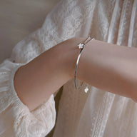 Bracelet fin en argent sterling avec étoile scintillante, porté sur poignet féminin en blouse blanche brodée.