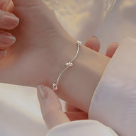 Bracelet fin en argent sterling avec trois petits nœuds perlés délicats sur poignet féminin.