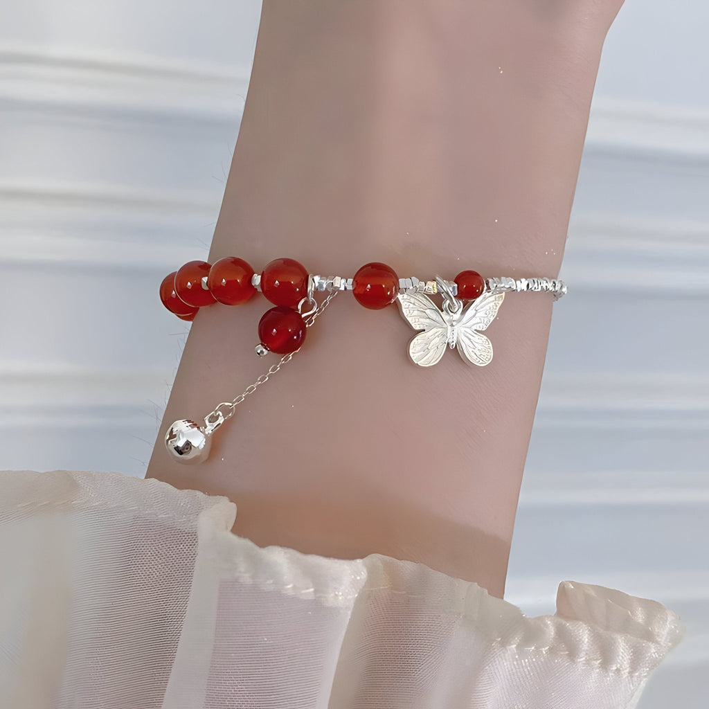 Bracelet argent sterling avec perles d'agate rouge et pendentif papillon sur poignet féminin.