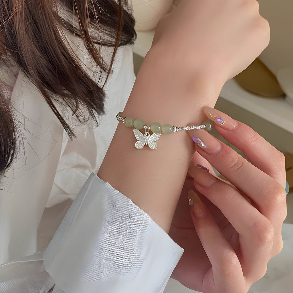 Bracelet en argent sterling avec pierres de jade vert clair et pendentif papillon blanc porté au poignet féminin.