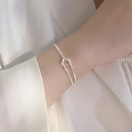 Bracelet en argent sterling avec design minimaliste à nœud délicat porté au poignet féminin.