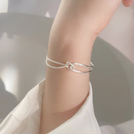 Bracelet fin en argent sterling avec petit nœud minimaliste porté au poignet féminin.