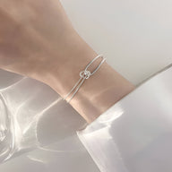 Bracelet fin en argent sterling à double chaîne avec petit nœud minimaliste sur poignet féminin.