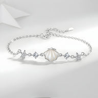 Bracelet en argent sterling avec charms coquillage nacré et étoiles de mer délicates, fermoir ajustable.