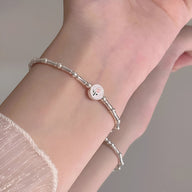 Bracelet en argent sterling avec petits maillons cylindriques et charm tulipe délicat sur poignet féminin.